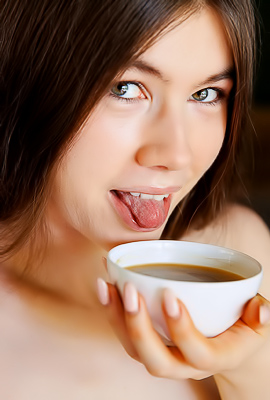 Bending over a chair, Marichka Glory spreads her legs wide while holding a cup, nude in a dim bedroom